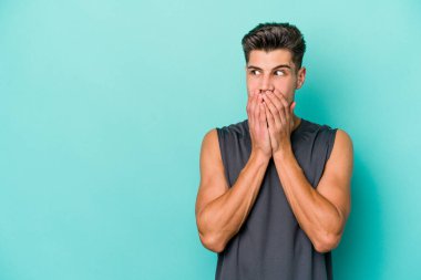 Kafkasyalı genç adam mavi arka planda izole edilmiş. Düşünceli bir şekilde ağzıyla ağzını kapatan bir fotokopi odasına bakıyor..