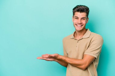 Mavi arka planda izole edilmiş genç beyaz bir adam palmiyesinde bir kopya alanı tutuyor..