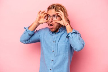 Pembe arka planda izole edilmiş genç beyaz adam bir başarı fırsatı bulmak için gözlerini açık tutuyor..