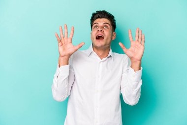 Kafkasyalı genç adam mavi arka planda izole edilmiş gökyüzüne haykırıyor, yukarı bakıyor, hayal kırıklığına uğramış..