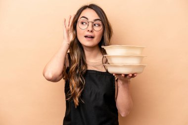 Beyaz tenli genç bir kadın bej arka planda saklanmış vaziyette bir dedikoduyu dinlemeye çalışıyor..