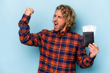 Mavi arka planda izole edilmiş pasaport taşıyan genç beyaz adam zaferden sonra yumruğunu kaldırıyor, kazanan konsept..