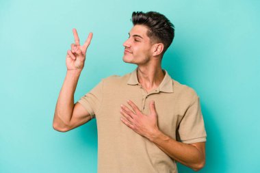 Kafkasyalı genç adam mavi arka planda izole edilmiş yemin ediyor, elini göğsüne koyuyor..