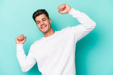 Mavi arka planda izole genç beyaz adam özel bir günü kutluyor, atlıyor ve enerjiyle kollarını kaldırıyor..