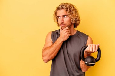 Genç sporcu halter sarı arka planda izole haldeyken şüpheli ve şüpheci bir ifadeyle yana bakıyor..