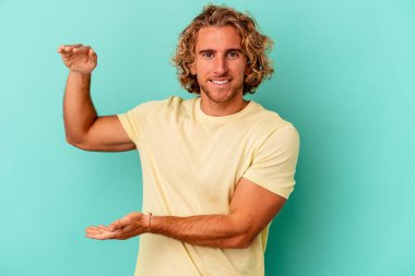 Kafkasyalı genç adam mavi arka planda izole edilmiş. Elinde işaret parmaklarıyla küçük bir şey tutuyor, gülümsüyor ve kendinden emin..