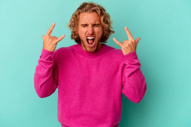 Mavi arka planda izole edilmiş genç beyaz adam boynuzlarını devrim konsepti olarak gösteriyor..