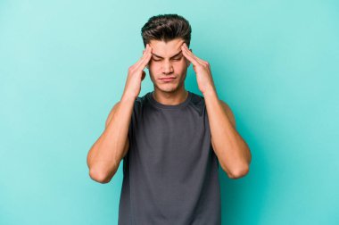 Genç beyaz adam mavi arka planda izole edilmiş tapınaklara dokunuyor ve başı ağrıyor..