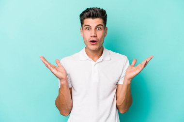 Kafkasyalı genç adam mavi arka planda izole edildi. Şaşırdı ve şok oldu..