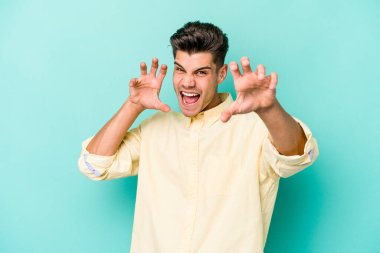 Mavi arka planda izole edilmiş genç beyaz adam gergin elleriyle çığlık atıyor..