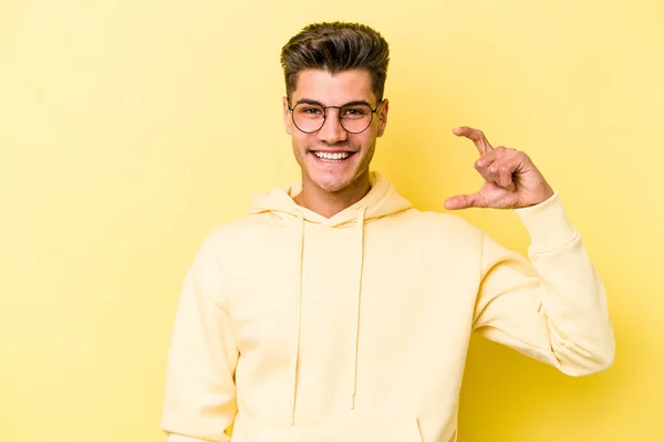 Mladý Běloch Izolovaný Žlutém Pozadí Drží Něco Málo Ukazováčky Usmívá — Stock fotografie