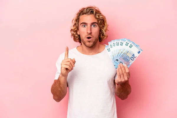 Young caucasian man holding banknotes isolated on pink background having some great idea, concept of creativity.