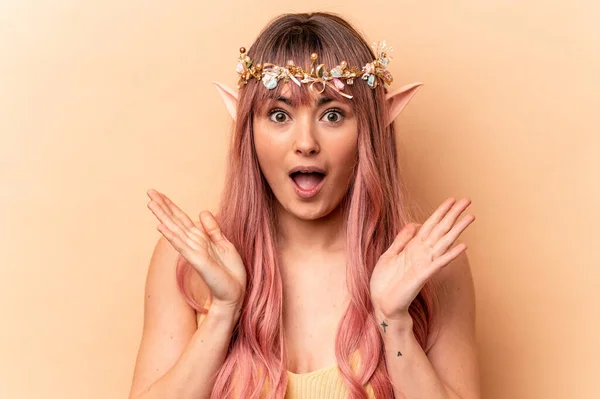Young elf woman with pink hair isolated on beige background surprised and shocked.