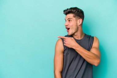 Kafkasyalı genç adam mavi arka plan noktalarında izole edilmiş başparmak uzakta, gülüyor ve kaygısız.