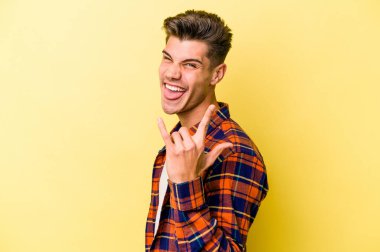 Sarı arka planda izole edilmiş genç beyaz adam parmaklarıyla kaya hareketi gösteriyor.