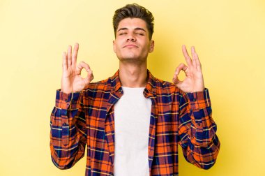 Sarı arka planda izole edilmiş genç beyaz adam sıkı çalışma gününden sonra rahatlıyor. Yoga yapıyor..