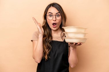 Beyaz tenli genç bir kadın bej arka planda saklanmış vaziyette. Şaşırmış ve şok olmuş..