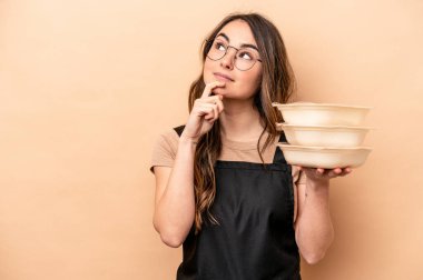 Beyaz tenli genç bir kadın bej arka planda saklanmış, şüpheli ve şüpheci bir ifadeyle yana bakıyor..