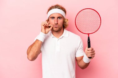 Badminton oynayan beyaz bir adam pembe arka planda izole edilmiş ve dudakları dudaklarında bir sır saklıyor..