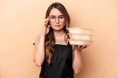 Beyaz tenli genç bir kadın bej arka planda saklanmış vazifesine odaklanmış, parmağıyla tapınağı işaret ediyor..