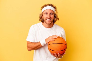 Genç basketbolcu beyaz adam sarı arka planda izole edilmiş gülüyor ve eğleniyor..