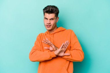 Kafkasyalı genç adam mavi arka planda izole edilmiş bir şekilde inkar hareketi yapıyor.