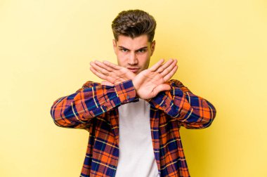 Sarı arka planda izole edilmiş genç beyaz adam inkar jesti yapıyor.