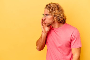 Sarı arka planda izole edilmiş genç beyaz bir adam gizli bir sıcak fren haberi veriyor ve yana bakıyor.