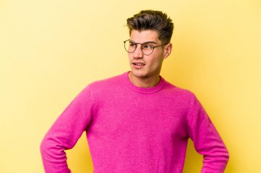 Sarı arka planda izole edilmiş genç beyaz adam şaşkın, şüpheli ve güvensiz hissediyor..