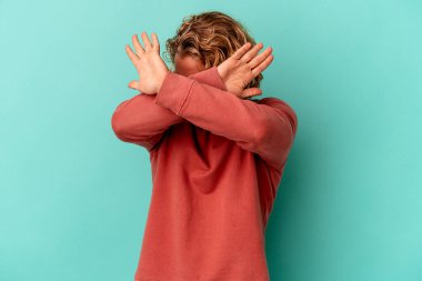 Kafkasyalı genç adam mavi arka planda izole edilmiş iki kolu çapraz tutuyor, inkar kavramı.