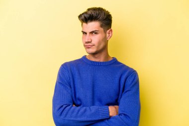 Genç beyaz adam sarı arka planda izole edilmiş şüpheli, belirsiz, seni muayene ediyor..