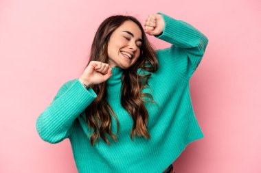 Pembe arka planda soyutlanmış genç beyaz bir kadın özel bir günü kutluyor, atlıyor ve enerjiyle kollarını kaldırıyor..