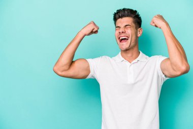 Mavi arka planda izole edilmiş genç beyaz bir adam zaferden sonra yumruğunu kaldırıyor, kazanan konsept..