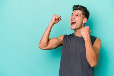 Mavi arka planda izole edilmiş genç beyaz bir adam zaferden sonra yumruğunu kaldırıyor, kazanan konsept..