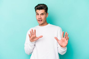 Mavi arka planda izole edilmiş genç beyaz adam tiksinti belirtisi gösteren birini reddediyor..