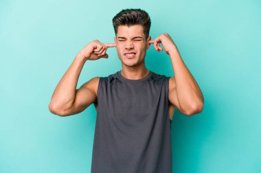 Genç beyaz adam mavi arka planda izole edilmiş parmaklarıyla kulaklarını kapatıyor, gürültülü bir ortam tarafından stresli ve umutsuz..