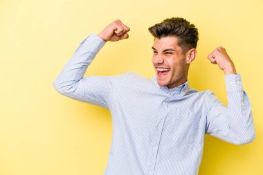 Sarı arka planda izole edilmiş genç beyaz adam zaferden sonra yumruğunu kaldırıyor, kazanan konsept..