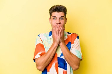 Sarı arka planda izole edilmiş genç beyaz adam elleriyle ağzını kapatırken şok oldu..