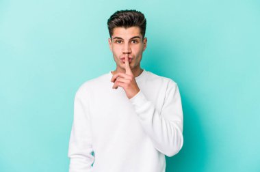 Mavi arka planda izole edilmiş genç beyaz bir adam ya sır saklıyor ya da sessizlik istiyor..
