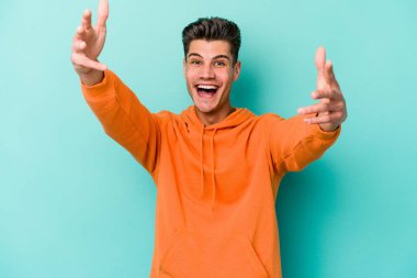 Mavi arka planda izole edilmiş genç beyaz bir adam zaferi ya da başarıyı kutluyor, şaşırıyor ve şok oluyor..