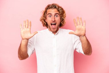 Pembe arka planda izole edilmiş genç beyaz adam hoş bir sürpriz alıyor, heyecanlı ve el kaldırıyor..