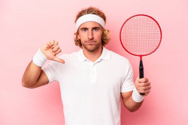 Badminton oynayan genç beyaz bir adam pembe arka planda izole edilmiş, hoş olmayan bir jest gösteriyor. Anlaşmazlık konsepti.