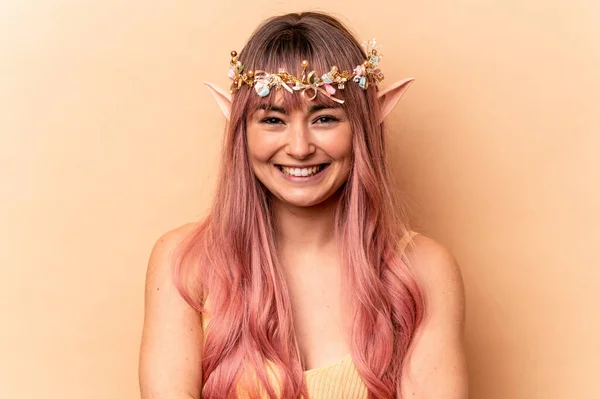 Young elf woman with pink hair isolated on beige background laughing and having fun.