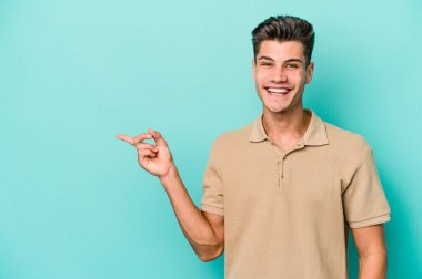 Mavi arka planda izole edilmiş genç beyaz adam işaret parmağıyla işaret ederek gülümsüyor..