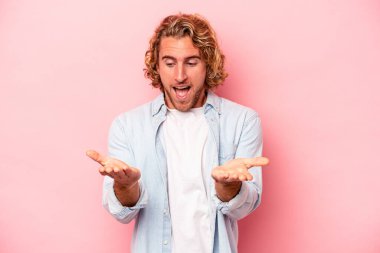 Pembe arka planda izole edilmiş genç beyaz bir adam elinde avuç içi bir şeyle kameraya sunuyor..