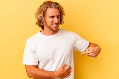 Sarı arka planda karaciğer ağrısı çeken, karnı ağrıyan genç beyaz bir adam..