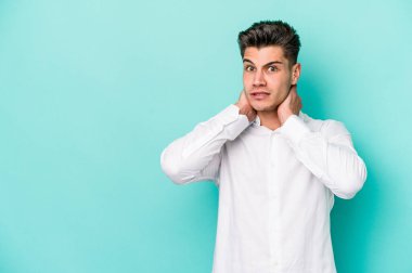 Kafkasyalı genç adam mavi arka planda izole edilmiş kafasının arkasına dokunuyor, düşünüyor ve bir seçim yapıyor..
