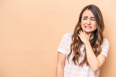 Kafkasyalı genç bir kadın bej arka planda izole edilmiş kafasının arkasına dokunuyor, düşünüyor ve bir seçim yapıyor..