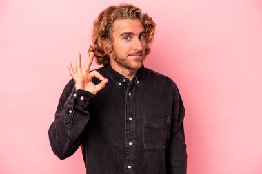 Pembe arka planda izole edilmiş genç beyaz bir adam bir göz kırptı ve elleriyle iyi bir jest yaptı..