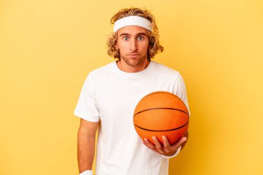 Genç basketbolcu beyaz adam sarı arka planda izole edilmiş omuzlarını silkeliyor ve gözleri açık..